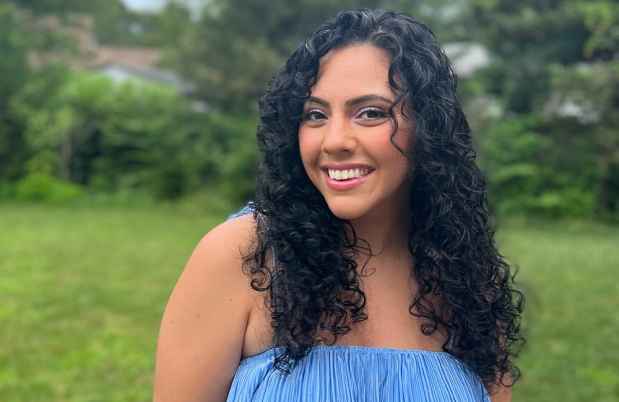 Participant Irene - person with long and wavy dark hair wearing blue and smiling outside