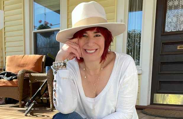 Participant Jen - person with red hair wearing a large hat smiling in front of a doorway
