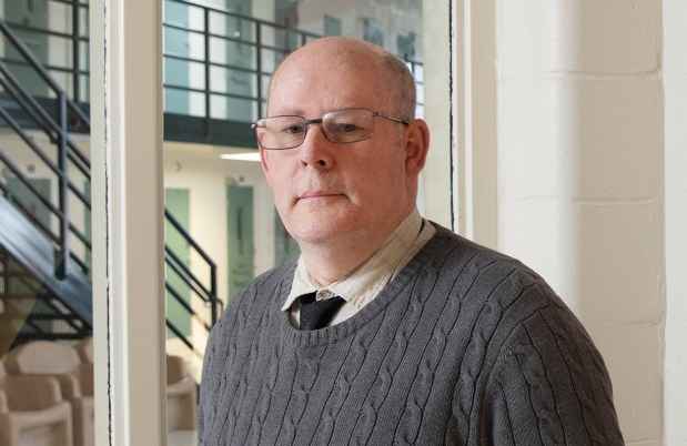 Participant John - person with glasses wearing a grey sweater in front of an office window