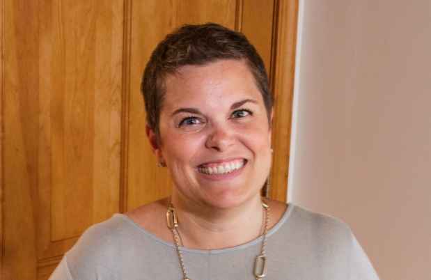 Participant Ann - person with short brown hair smiling in front of a beige wall
