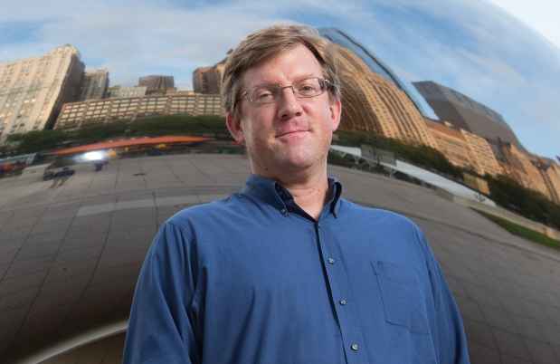 Participant John - person with short brown hair and glasses smiling in front of a large mirrored surface 