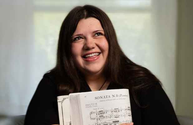 Participant Ashley - person with long dark hair smiling and holding sheet music