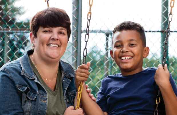 Participant Jennifer - person with short dark hair smiling with a child on a swing set