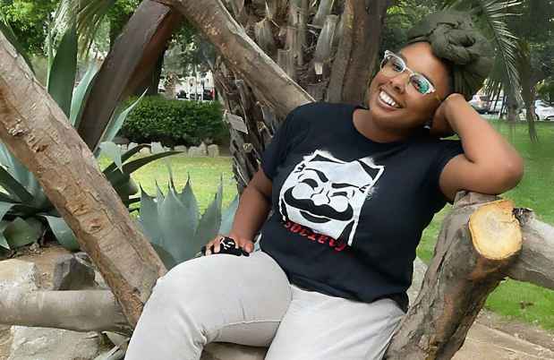 Participant Chezia sitting outside wearing a black t-shirt smiling