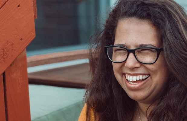 Participant Dayna - person with long and dark wavy hair and glasses smiling