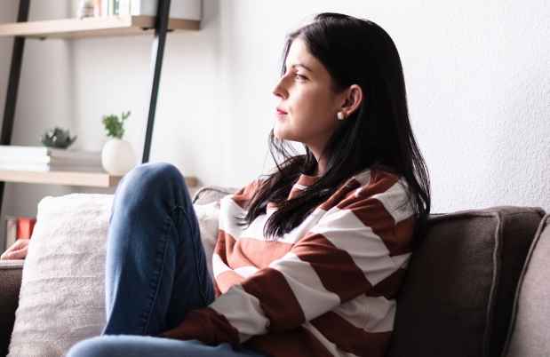 Person sits on couch with knee up looking out window