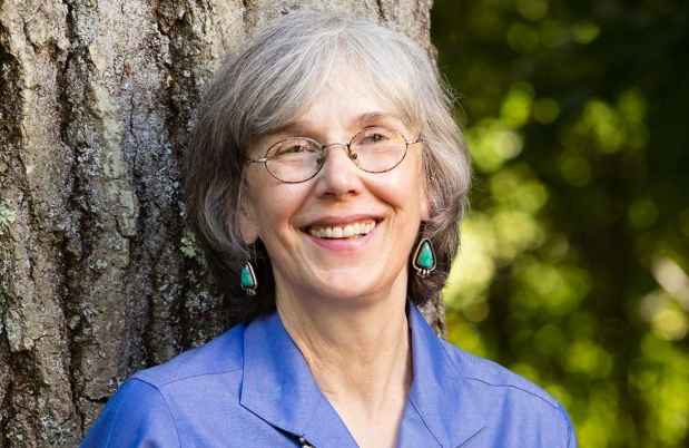 Participant Luanna - person with short grey hair smiling against a big tree trunk