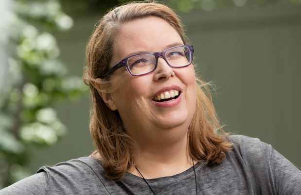 Participant Laura with blonde hair and glasses is sitting in a chair outside smiling
