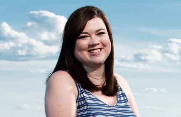 Participant Clare - person with long dark hair smiling in front of a blue sky