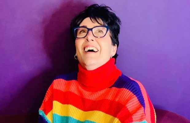 Deconstructing Stigma participant Tami - person in rainbow sweater sits on purple plush chair looking up