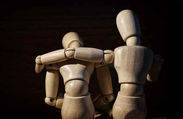 Artist mannequins posed on an embrace of support, black background