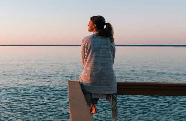 Woman sits on railing, looking out to sea