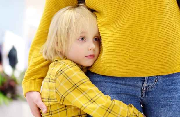 Child holds parent leg, looks worried