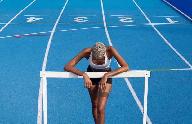Athlete leans on hurdle on blue track
