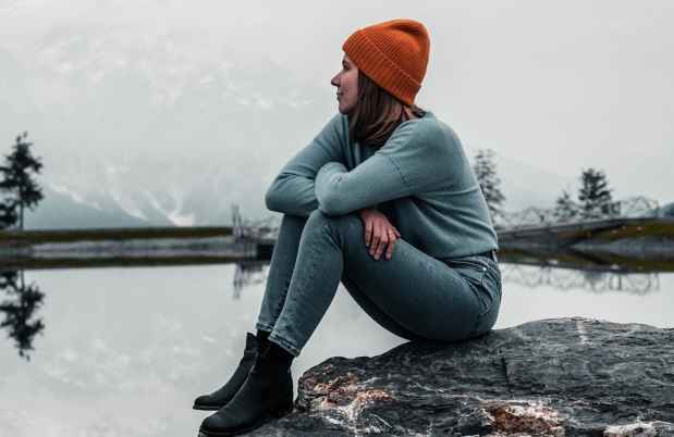 Person sits on rock looking out at lake in gray winter