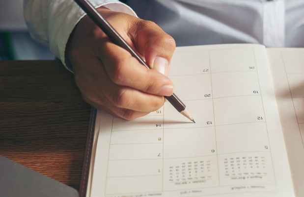 Hand holding smartphone, the other writing in calendar