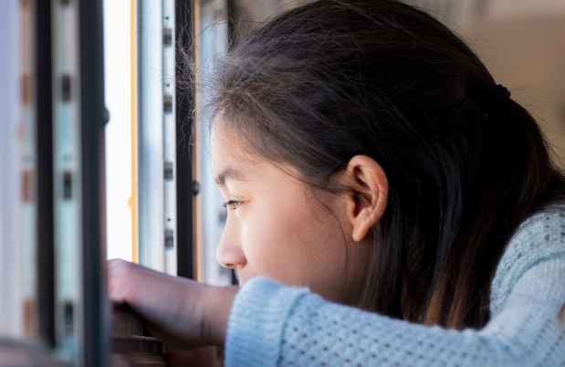 Girl with long dark hair looking out an open school bus window