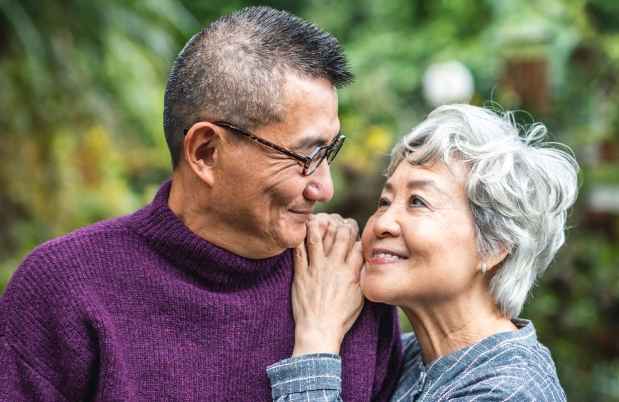 Two older adults looking lovingly at one another outside among greenery