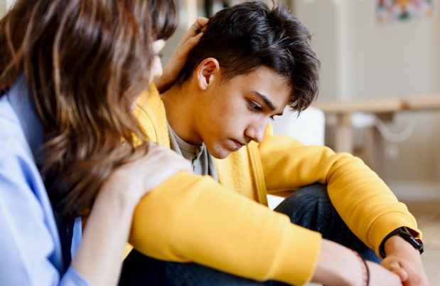 Boy sits, looking down, and a woman comforts him