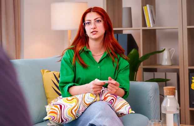 Person with bright red hair wearing a green shirt and sitting on a couch