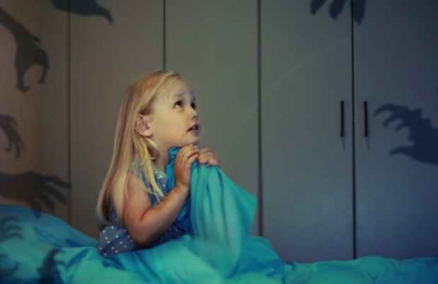 Young girl sits in bed surrounded by shadows of monsters