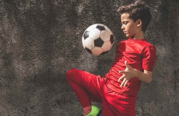 Boy in a red soccer uniform playing with a soccer ball