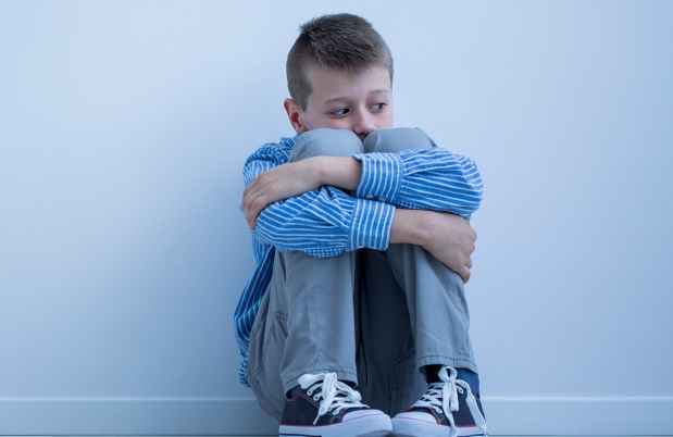 Young boy sits against wall, knees up