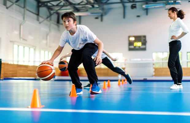Teen practicing basketball skills in a school gym
