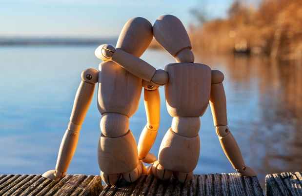 Two wooden figures sitting together by a body of water