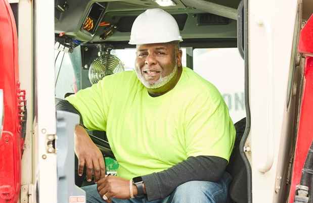 Deconstructing Stigma participant Julian - person in safety yellow shirt and hard hat in construction vehicle