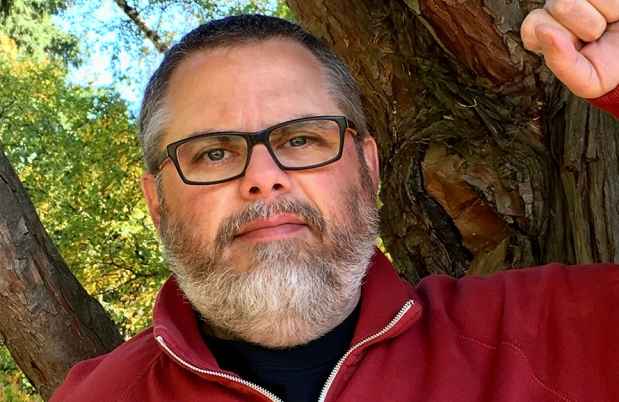 Deconstructing Stigma participant Noal - person in red zip up and glasses leans on tree