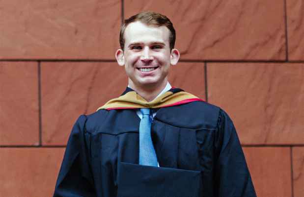 Deconstructing Stigma participant Scott - person poses in front of wall in graduation gown