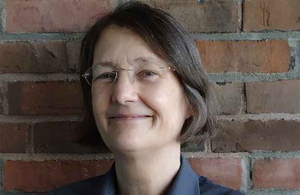 Deconstructing Stigma participant Lisa - person with shoulder length hair and glasses leans on brick wall