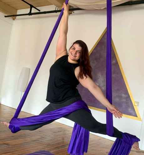 Participant Amanda suspended from the ceiling by purple aerial scarfs