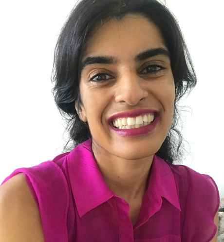 Participant Samina - person with dark wavy hair wearing a pink shirt smiling in front of a white background