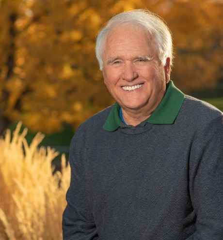 Participant Mike - person with short white hair smiling in front of fall foliage