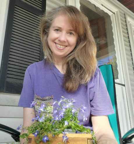Participant Phyllis - person with long light brown hair smiling with a box of purple flowers