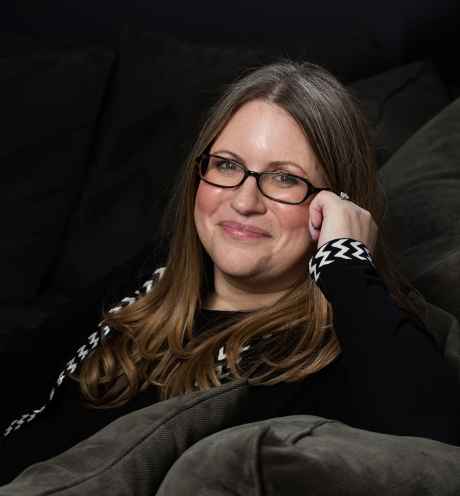 Participant Miriam - person with brown hair and glasses in front of a dark background