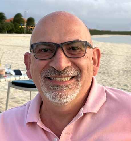 Participant Steve - person with grey facial hair wearing glasses and a pink shirt smiling on a beach