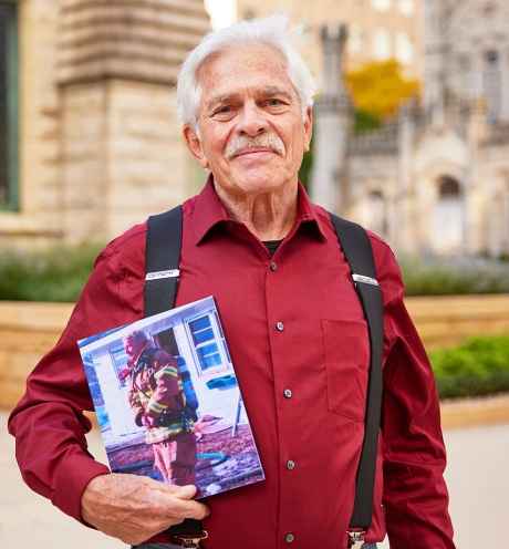 Participant Al - person with short white hair and a red shirt standing outside holding a framed photo