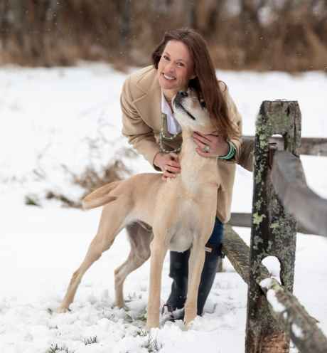 Participant Ashley - person with auburn hair smiling and hugging a dog outside