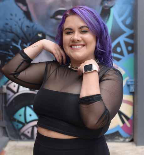 Participant Joanne - person with purple hair smiling in front of a colorfully painted wall