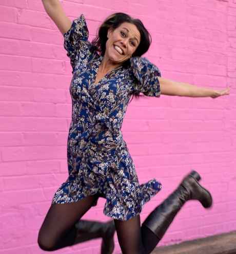 Participant Jen - person with long dark hair smiling and jumping in front of a pink background