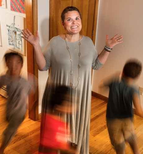Participant Ann - person with short brown hair smiling in front of a beige wall, children are running around