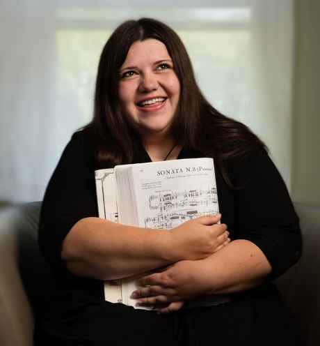 Participant Ashley - person with long dark hair smiling and holding sheet music