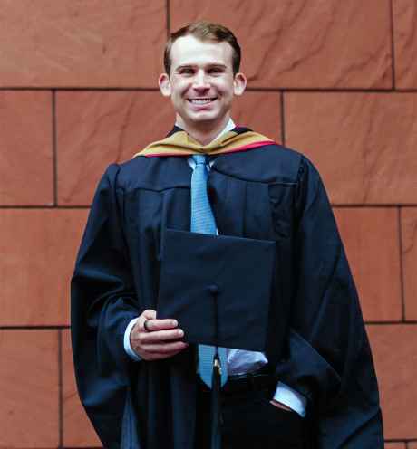 Deconstructing Stigma participant Scott - person poses in front of wall in graduation gown