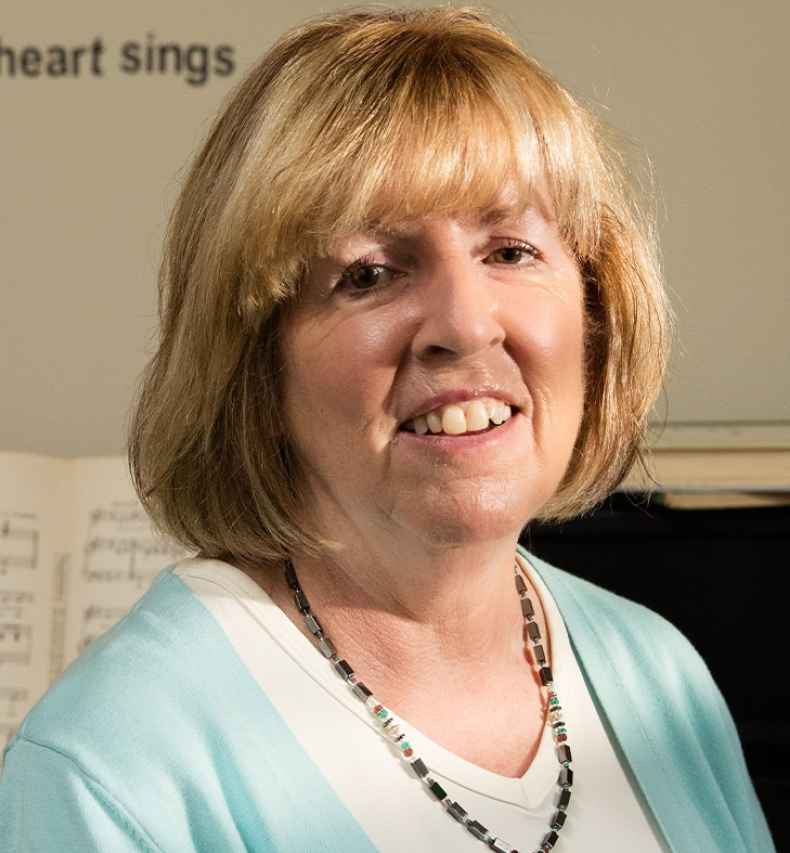 Participant Lisa - person with blond hair in a blue sweater sitting in front of a piano