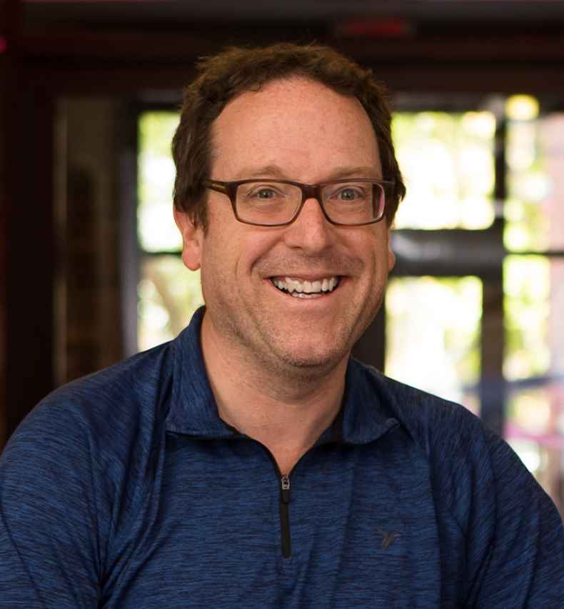 Participant Thomas - person with short brown hair and glasses smiling in a hallway with red lighting
