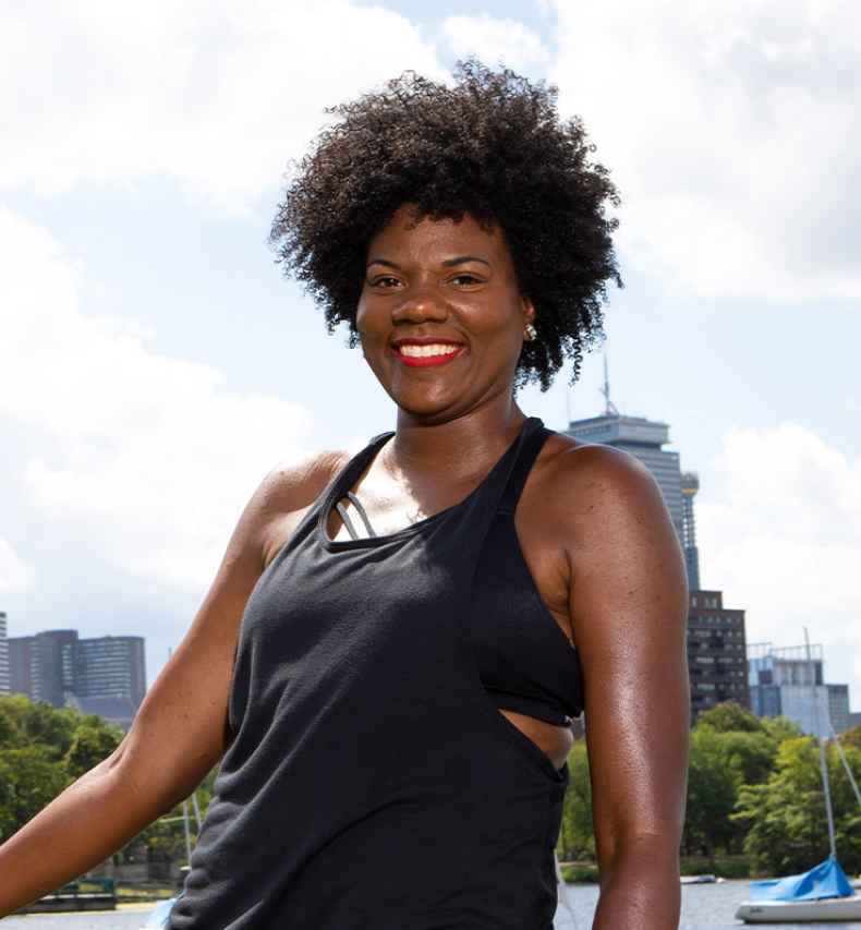 Participant Nieisha - person with dark curly hair smiling in front of the Boston skyline