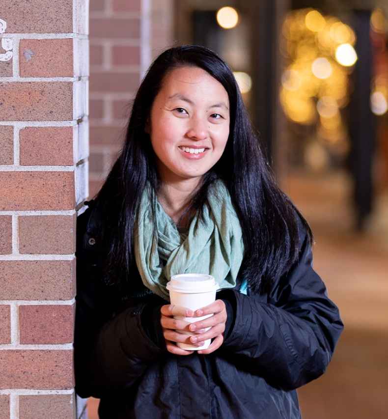 Participant Tian - person with long dark hair outside, there are trees with lights in the background
